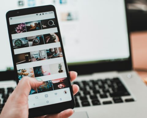 Auf dem Bild ist ein Smartphone im Vordergrund. Im Hintergrund ist ein Laptop zu sehen.